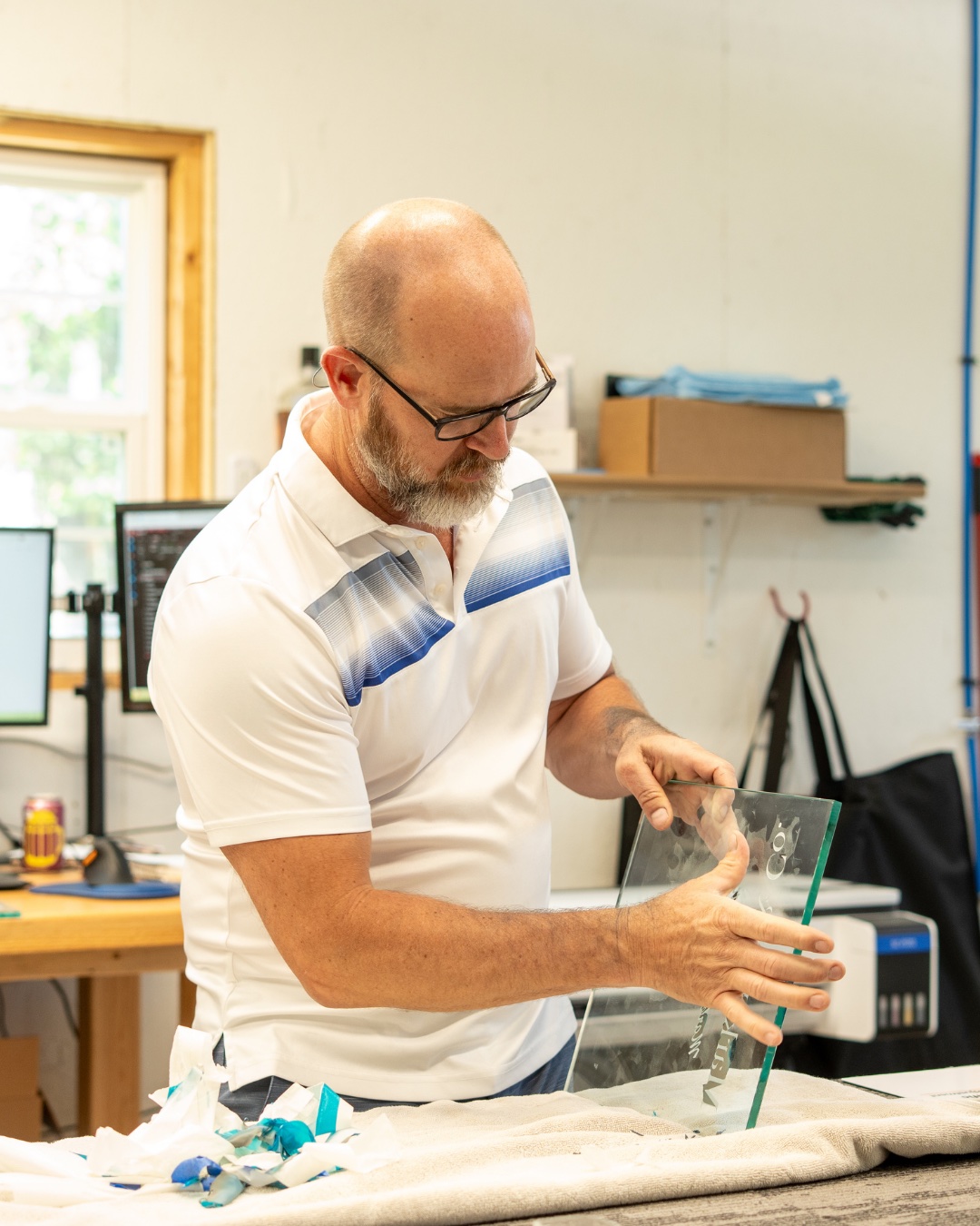 Kerry Dougan at the studio workbench, holding a sand-carved glass piece.